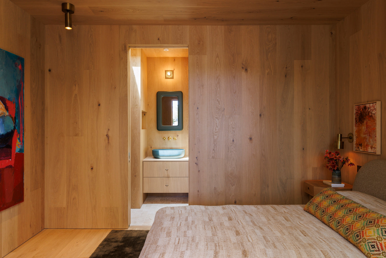 Continuous oak wall paneling by MADERA seamlessly connects bedroom to ensuite bathroom in this cohesive design.