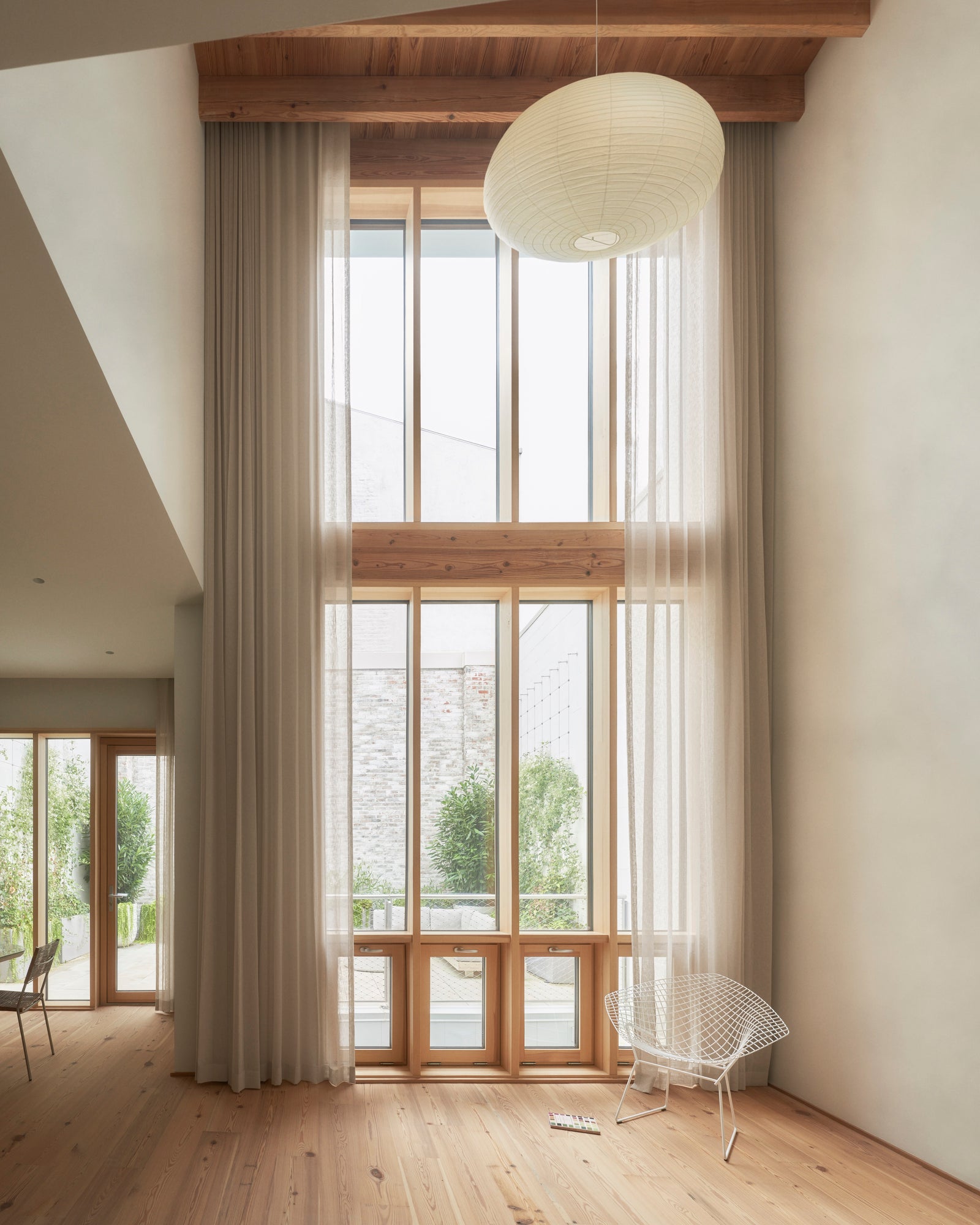 Soaring wood-framed windows stretch across two stories, connecting interior calm to exterior terraces with purposeful material continuity.