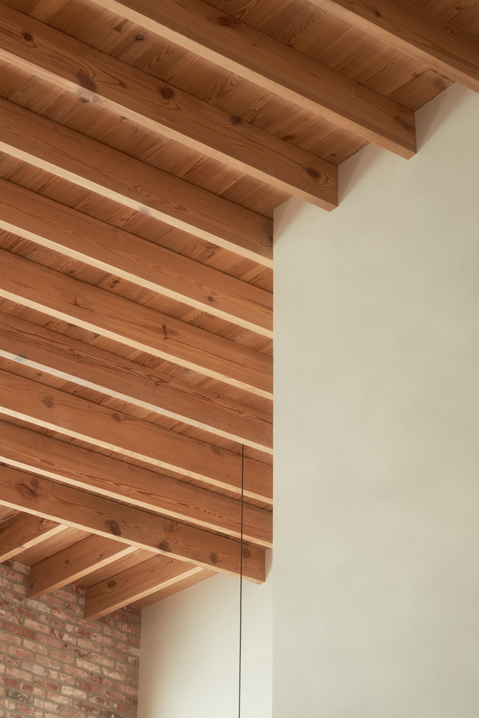 Exposed wood beams and planking create a cathedral effect overhead, their rhythmic pattern softening the building's industrial brick heritage.