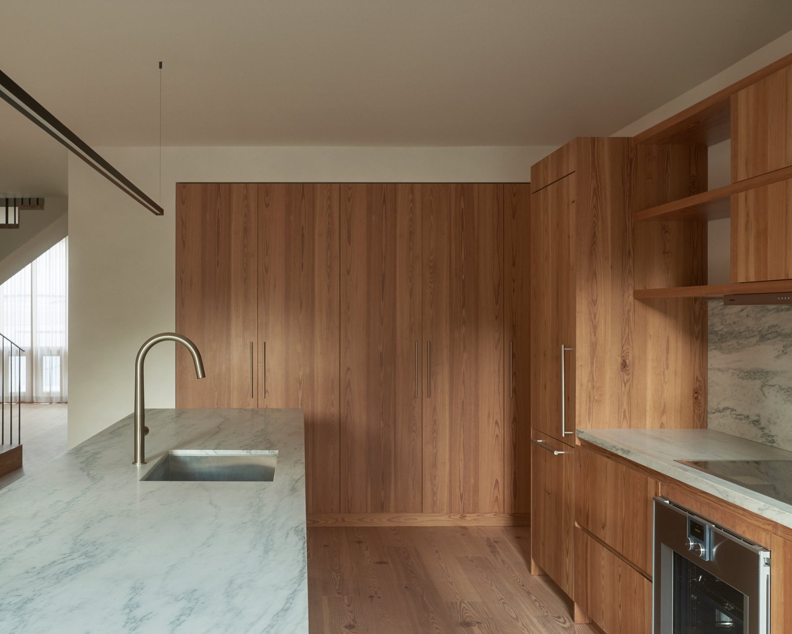 Floor-to-ceiling wood millwork defines the kitchen with restrained elegance, its consistent grain and tone unifying the open plan.