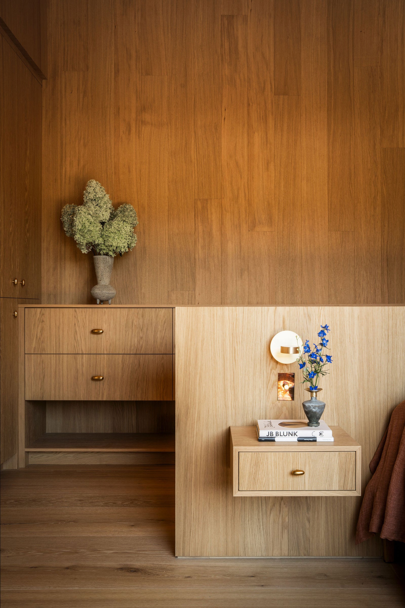 Thoughtful oak millwork, from wall paneling to floating nightstands, brings continuity and warmth to this serene bedroom.